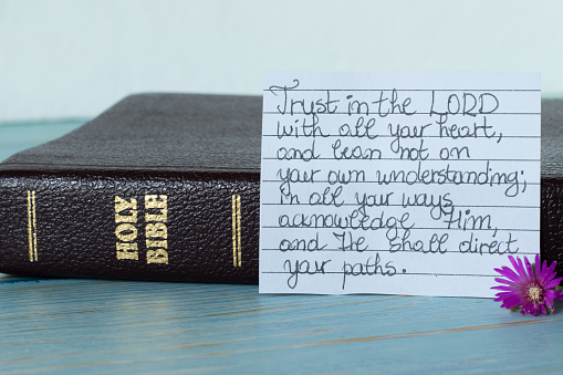 Closed Holy Bible Book and handwritten note to trust in the LORD with all your heart on wooden background. A close-up. Christian biblical concept.