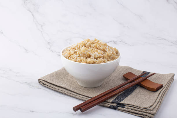 коричневый рис в белой рисовой миске выделен на белом фоне. - brown rice фотографии стоковые фото и изображения