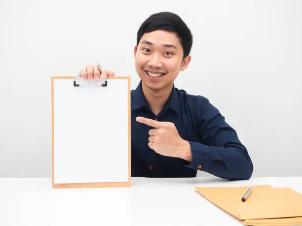Handsome man smile face sitting at the table and point finger at blank paper on woodboard white background