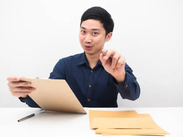 Asian man holding document woodboard and point pen at you,Businessman gesture choose you white background