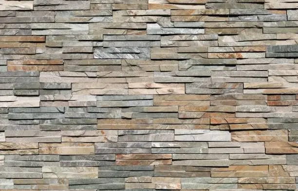 Photo of Stone cladding wall made by elongated bricks of natural multicolor rocks. Panels for exterior