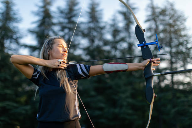 Outdoors archery training Woman practicing archery training with recurve bow on open field before sunset. She is in very good shape archery stock pictures, royalty-free photos & images