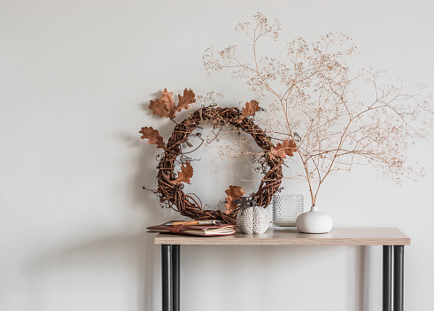 Cozy autumn home interior - a wreath with autumn leaves, dried flowers, a ceramic pumpkin on a wooden rack
