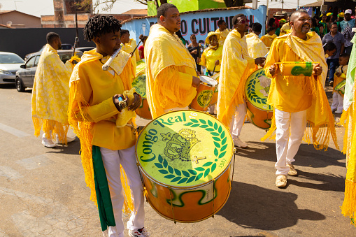 Goiânia, Goias, Brazil – September 11, 2022:  Some revelers dressed in yellow, playing percussion instruments, singing and dancing, during the Congadas in Goiânia, an Afro-Brazilian cultural and religious manifestation.