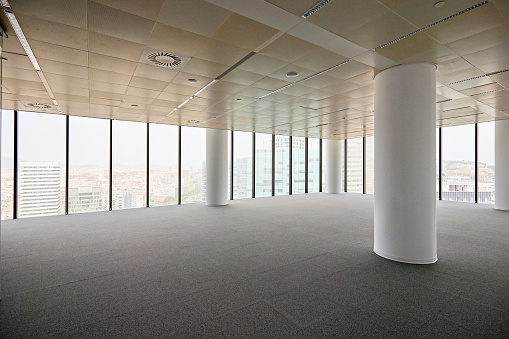 Unoccupied floor in multi-story building with carpeting, white architectural columns, and floor to ceiling windows with high angle perspective.
