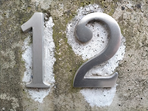 Number twelve,12 in metal number on a wall of the entrance of a house.