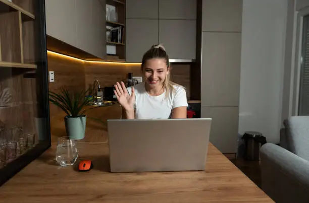 Young happy girl or woman talking on video call and waving with hand to her boyfriend who is on assignment as military soldier or medical worker doctor in foreign country. Freelancer woman online
