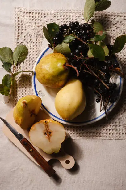 Ripe yellow pears and chokeberry on white plate prepared for jam cooking on rustical tablecloth, top view, flat lay.