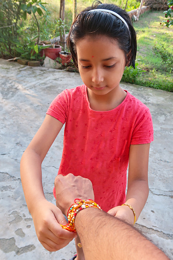 Stock photo showing close-up view of Indian girl taking part in the Hindu festival of brotherhood and love, Raksha Bandhan ceremony. During this annual event, held on the last day of the Hindu lunar calendar month of Shraavana, sisters tie a rakhi, string bracelet, on their brothers' wrists to signify protection.