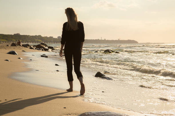 sad blond woman sad blond barefoot woman walking away at sunny sea beach, toned image walking beach women sadness stock pictures, royalty-free photos & images