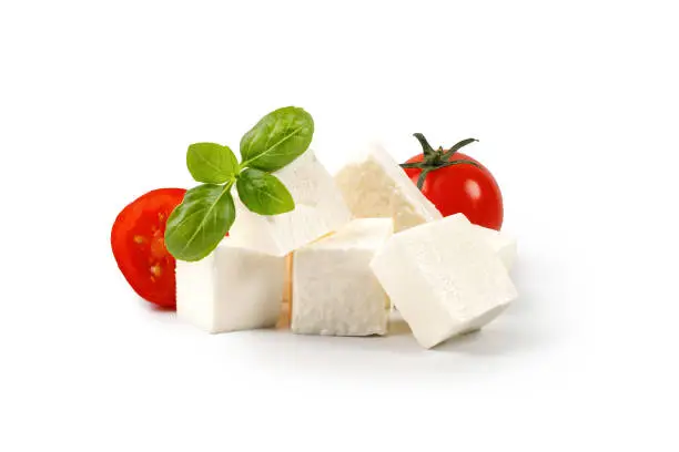Feta cheese cubes isolated on white background with clipping path. Heap of Feta cheese, basil leaves and tomatoes.