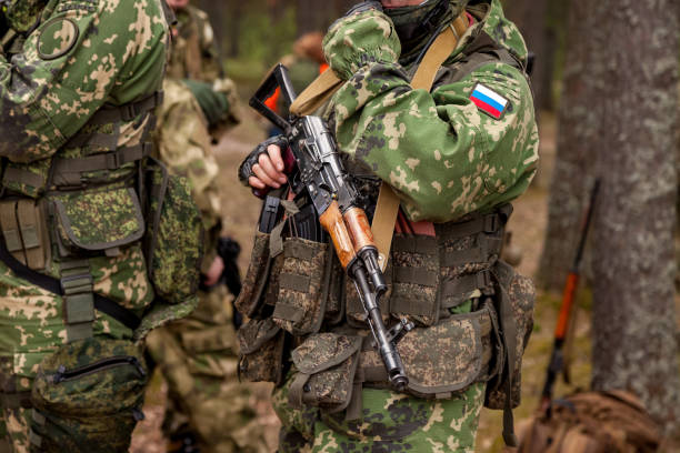 close up hands russian soldier man dressed military camouflage uniform holds weapon in woodland at soldiers background. male border guard in country border holding machine gun on war. copy text space - guerra imagens e fotografias de stock