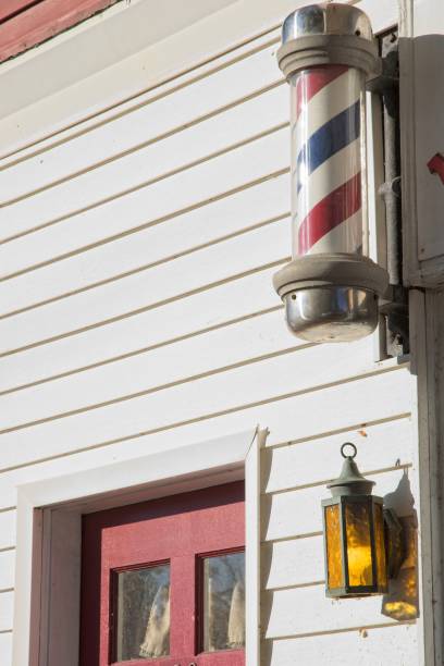 istock Barbers pole and lantern hung on building with white clapboard siding red door 1426283071