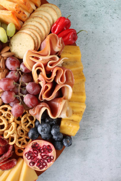 istock Close-up image Christmas charcuterie board ingredients, ham, crackers, red and white grapes, mini red bell peppers, pretzels, pomegranate, almonds, salami, blueberries, cheddar cheese, elevated view, copy space 1426283224