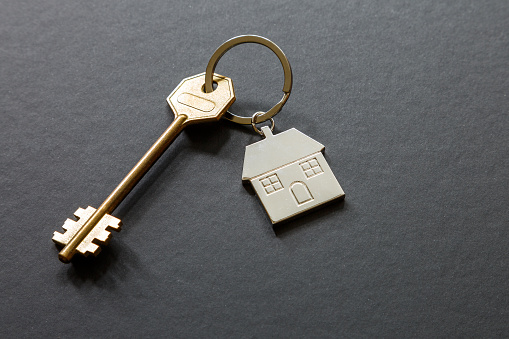 A key with a keychain in the form of a house on a black background. Space for text. The concept of buying, renting, home insurance.