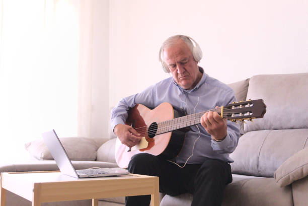 istock Concept learning within covid19 pandemics. Mature man with headphones learning to play guitar online with laptop alone at home. 1426284019