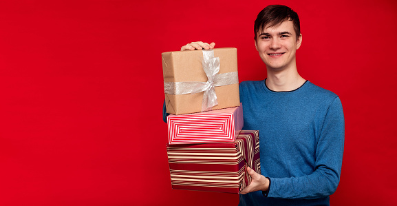 Young man with gifts in his hands on a red background. Concept holidays, Black Friday. Copy space