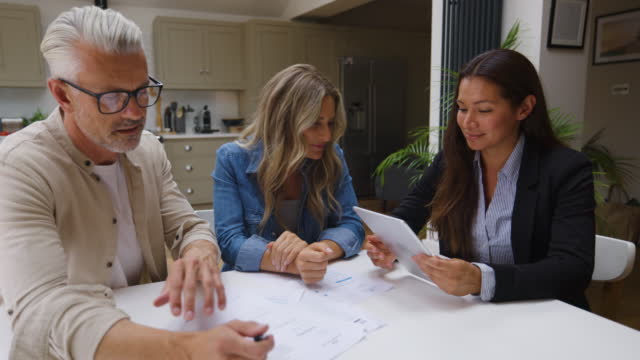 Heterosexual couple listening to their female financial advisor while she shows them information on tablet and documents