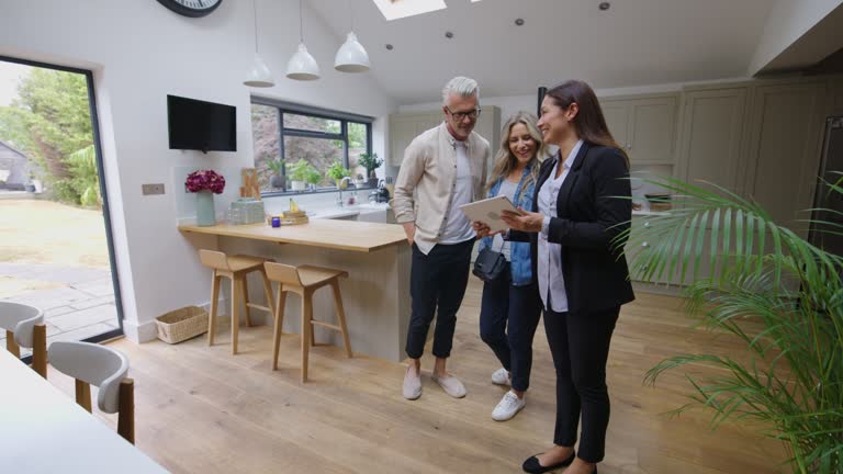 Caucasian mature couple looking at a property with female real estate agent while she shows them additional information on tablet