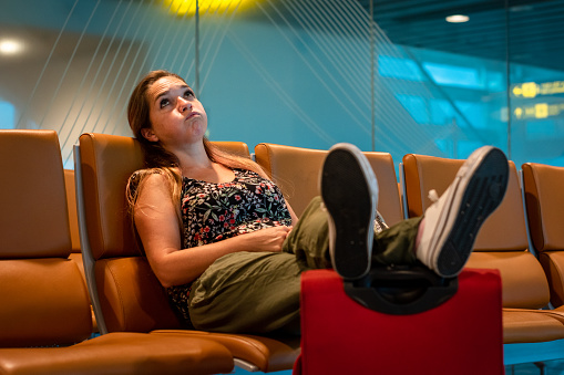 Young woman at the airport waiting for her flight to depart. Woman at the airport bored of waiting. Tired person at the airport. Delayed flight