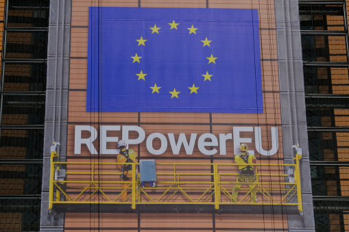 A row of back-lit flags in front of the glass facade of the Paul Henri Spaak building of the European Parliament in Brussels.\