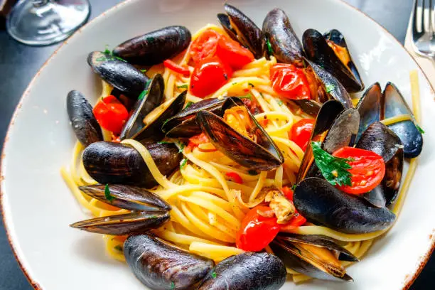 A white plate with a beautiful Italian dish of linguini with mussels and cherry tomatoes.