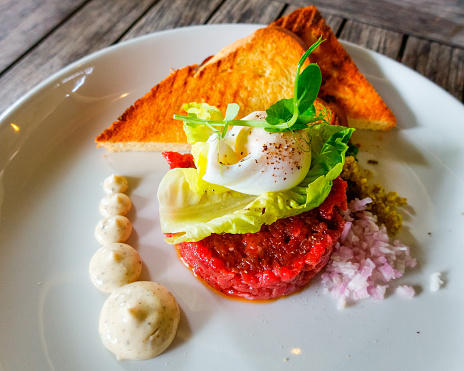 A white plate with a classic from the French cuisine: steak tartare with a poached egg.