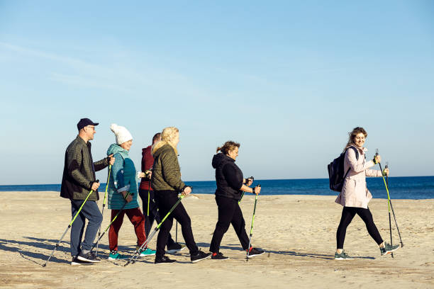 weibliche leiterin sportlerin und gruppe freude skandinavisches, nordic walking mit professionellen stöcken in der nähe von meer. leerzeichen kopieren - power walken stock-fotos und bilder