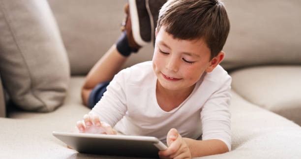 istock Digital tablet kid learning games, watching cartoons and internet online while relaxing on sofa at home. Happy curious young boy child playing on technology, fun modern app and educational connection 1426303128