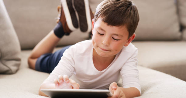 istock Digital tablet kid learning games, watching cartoons and internet online while relaxing on sofa at home. Curious young boy child playing on wifi technology, fun modern apps and educational connection 1426303142