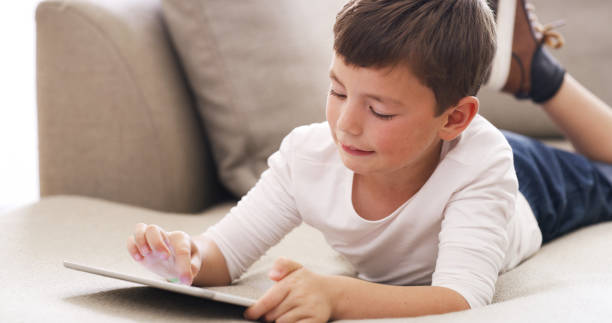istock Learning, education and boy with a digital tablet, playing educational game or streaming a lesson online while lying on a sofa. child having fun, relax and enjoying streaming or subscription service 1426303149