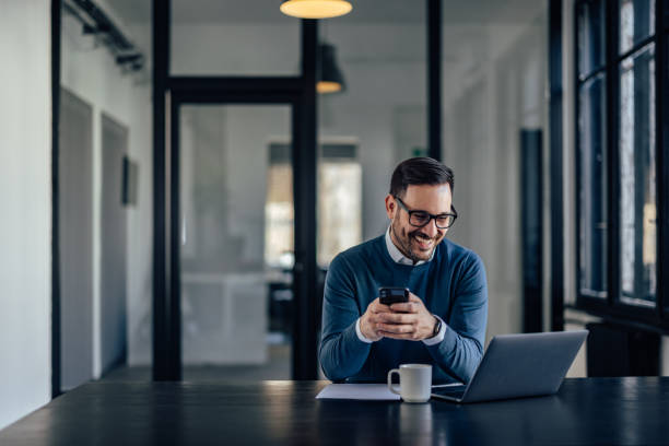 istock Smiling man holding a phone while looking at the laptop, at the office. 1426306849