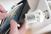 person holding wallet with cash next to turned down thermostat on radiator
