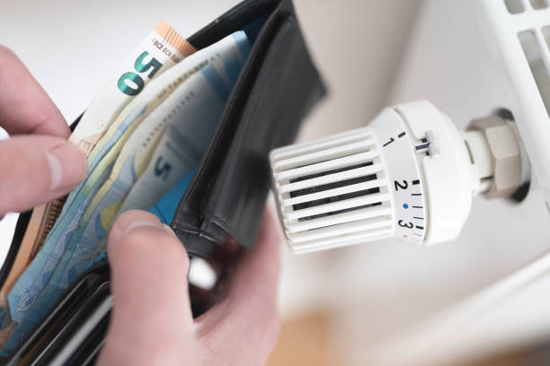 person holding wallet with cash next to turned down thermostat on radiator close-up view of person holding wallet with cash next to turned down thermostat on radiator, rising energy and heating costs concept home heating stock pictures, royalty-free photos & images