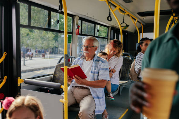 An elderly man is on the city bus reading a book