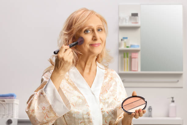istock Mature woman in a bathrobe applying make up using a brush in a bathroom 1426309322