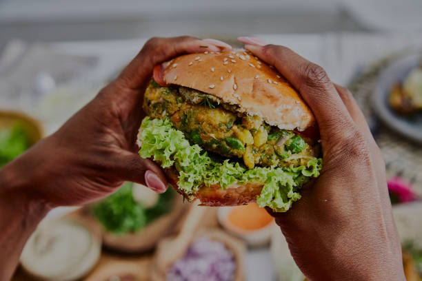 A woman holding a healthy vegan burger A woman holding a healthy vegan burger, made of green peas, chickpea, corn, fresh seasoning, herbs and spices veggie burger stock pictures, royalty-free photos & images