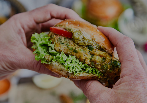 A man hands holding a healthy & tasty vegan hamburger, made of zucchini, green pea, seasoning, herbs and spices, with pesto sauce, close up