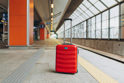 Forgotten travel bag on the train station. Red suitcase on empty station platform. Travel and vacation theme background.