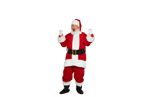 Portrait of senior man in image of Santa Claus posing with winning emotions isolated over white background. Concept of fictional character, holiday, New Year, Christmas. Copy space for ad