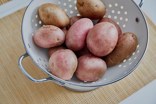 Fresh raw red potatoes in a white retro metal bowl, ready for food preparation and baking, close up macro, table top view