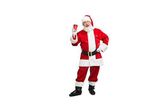 Portrait of senior man in image of Santa Claus isolated over white background. Coffee break. Concept of fictional character, holiday, New Year, Christmas. Copy space for ad