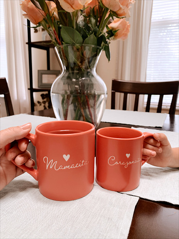 A Mother & Daughter's Hands Holding Matching Pink Mugs That Say 