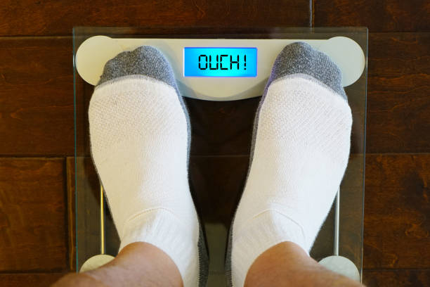 istock Man stand on the digital weight scale with humorous OUCH message. 1426332961