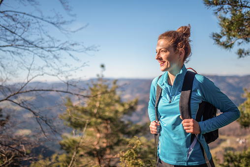 A Caucasian woman in her 30's wearing warm sports clothing and backpack as she pauses to enjoy the view.
