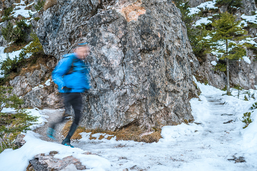 Unrecognizable Caucasian male trail runner wearing sports clothes and backpack, running in snowy nature.