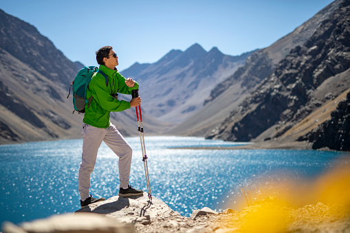 Hiker resting and enjoying the views of the Chilean Andes mountain range with the Lake of the Inca in the background, locally known as “Laguna del Inca”. The lake, which changes in colors from stunning emerald green to deep blue, can be viewed throughout the Portillo resort. It is often described as 