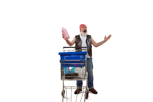 Portrait of senior man in leather vest standing with shopping trolley isolated over white background. Household goods. Concept of shopping, hypermarket, supermarket, purchasing. Copy space for ad