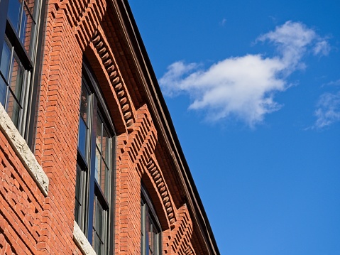 Detail of ornate brick work on old textile mill building converted to apartments. Cobalt blue sky background with puffy clouds contrast with architectural details.
