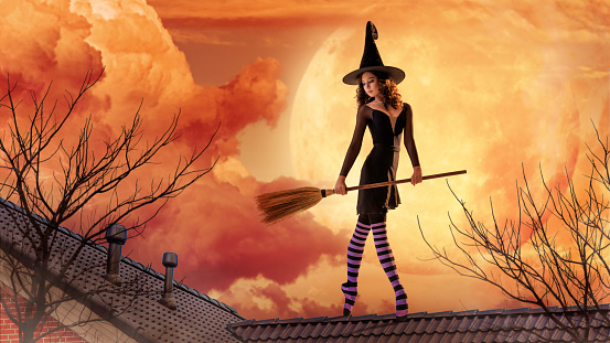 ballerina on pointe shoes in a black witch costume in a hat and with a broom dances on an orange background.